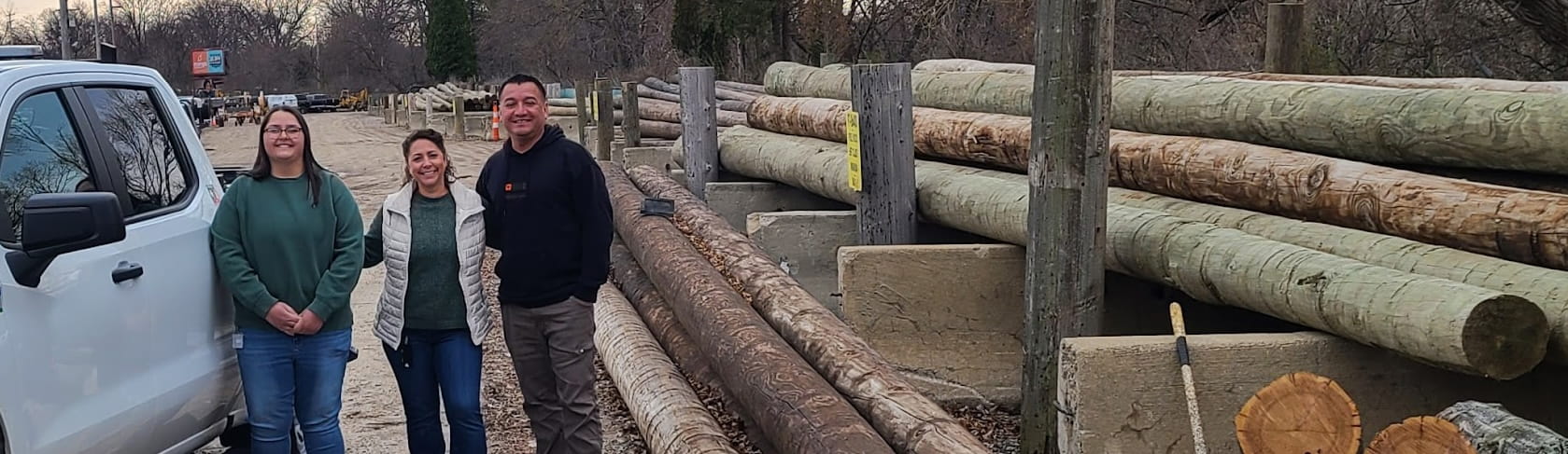 Pam posing with 2 people by some lumber